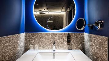 A bathroom with a white sink, granite tiles, a round mirror, and a blue accent wall.