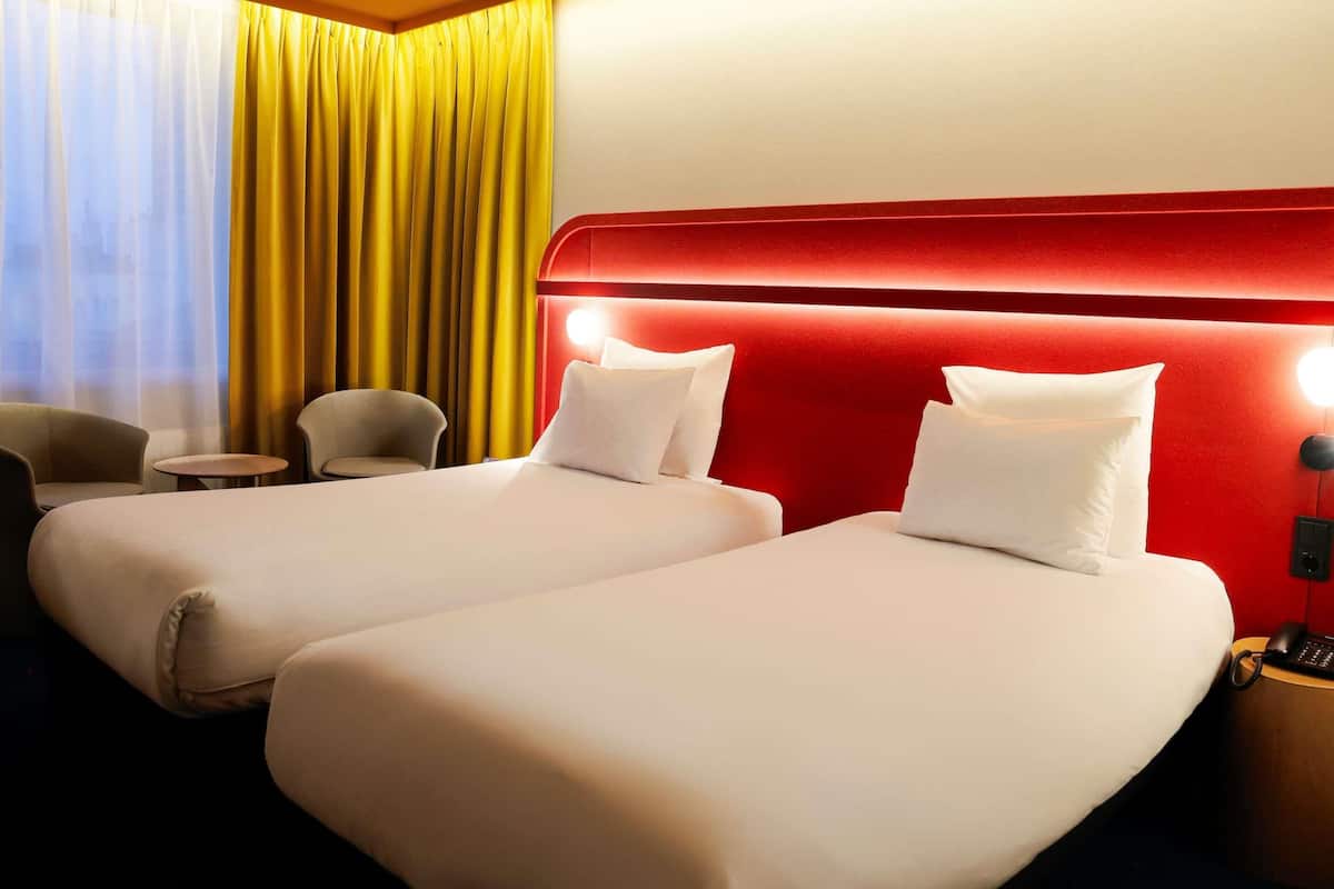 Habitación de hotel con dos camas, cabecero rojo, una mesita y una silla.