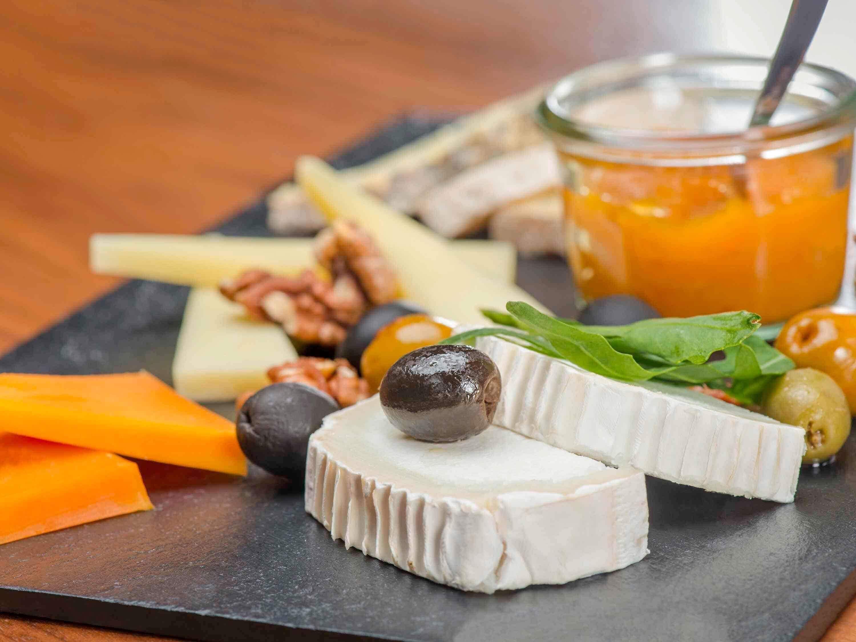 A charcuterie board with various cheeses, fruits, nuts, and a jar of jam.