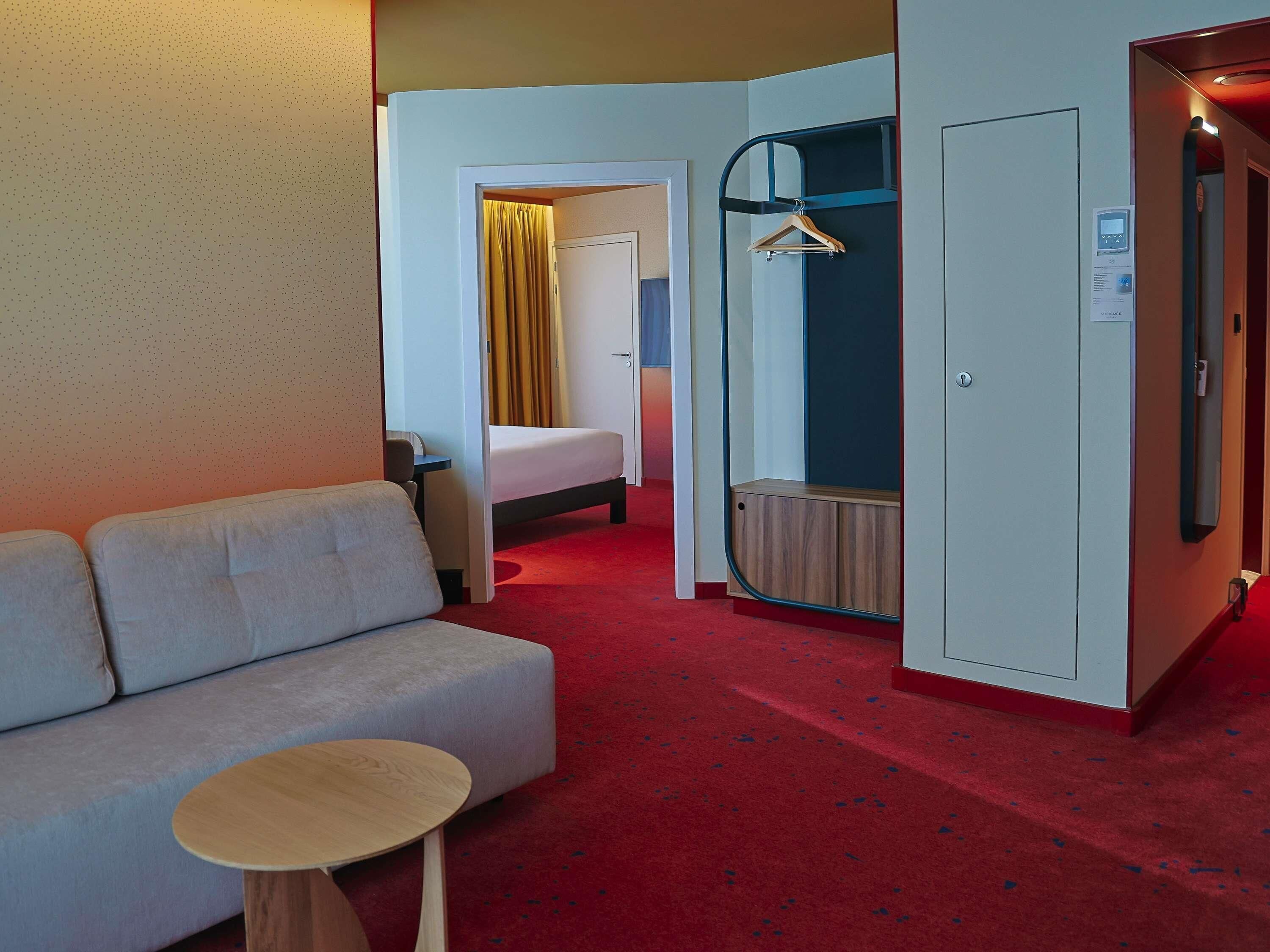 A hotel room with a sofa, a small round table, a bed, a wardrobe, and a mirror.