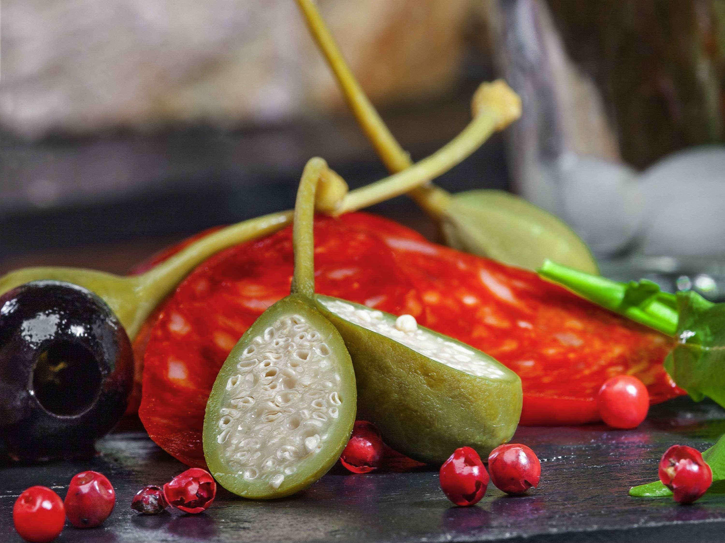 A variety of fruits and vegetables, including a sliced green fruit, red chili peppers, and red berries, arranged on a dark surface.