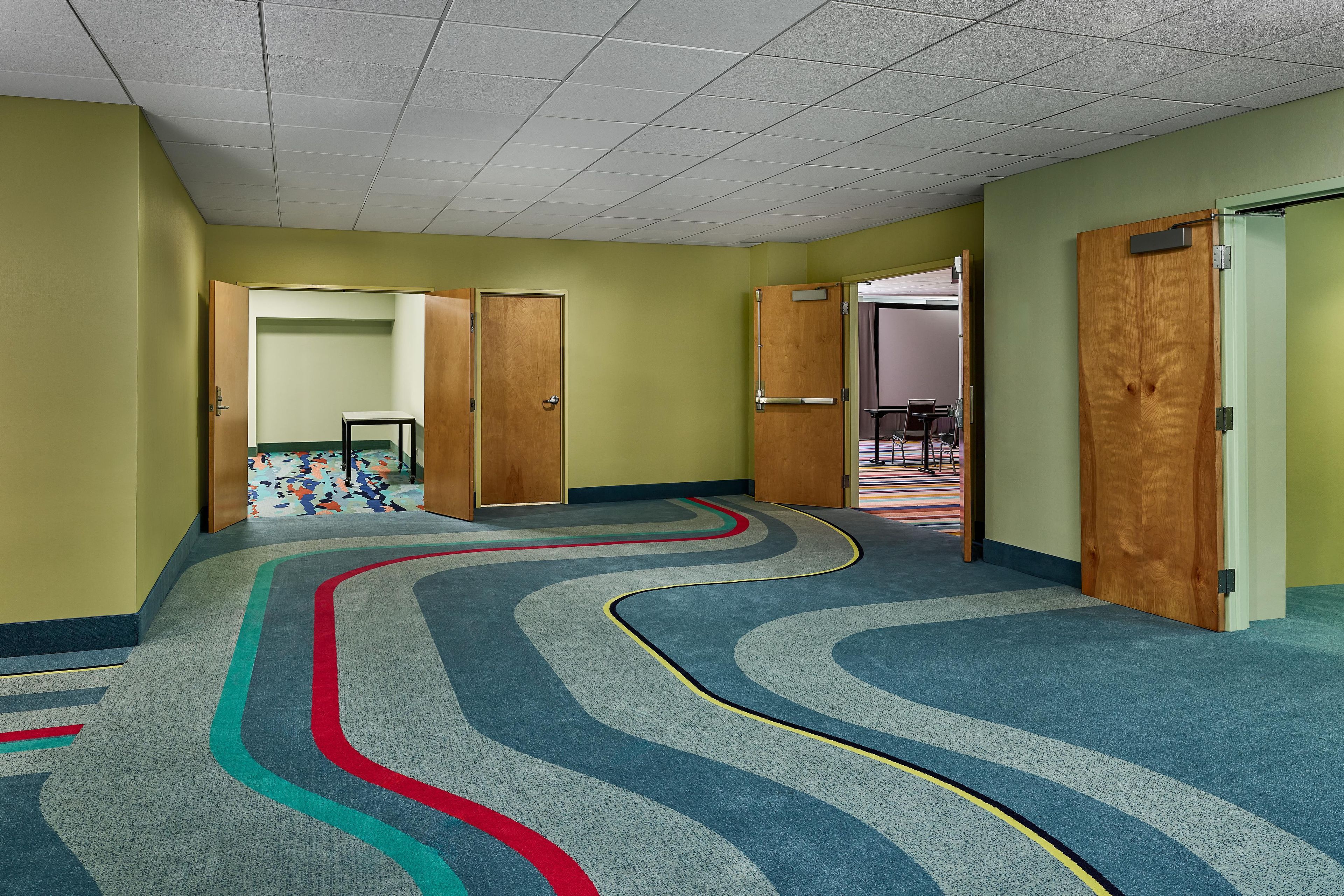 A hallway with carpeted flooring, wooden doors, and a colorful carpet design.