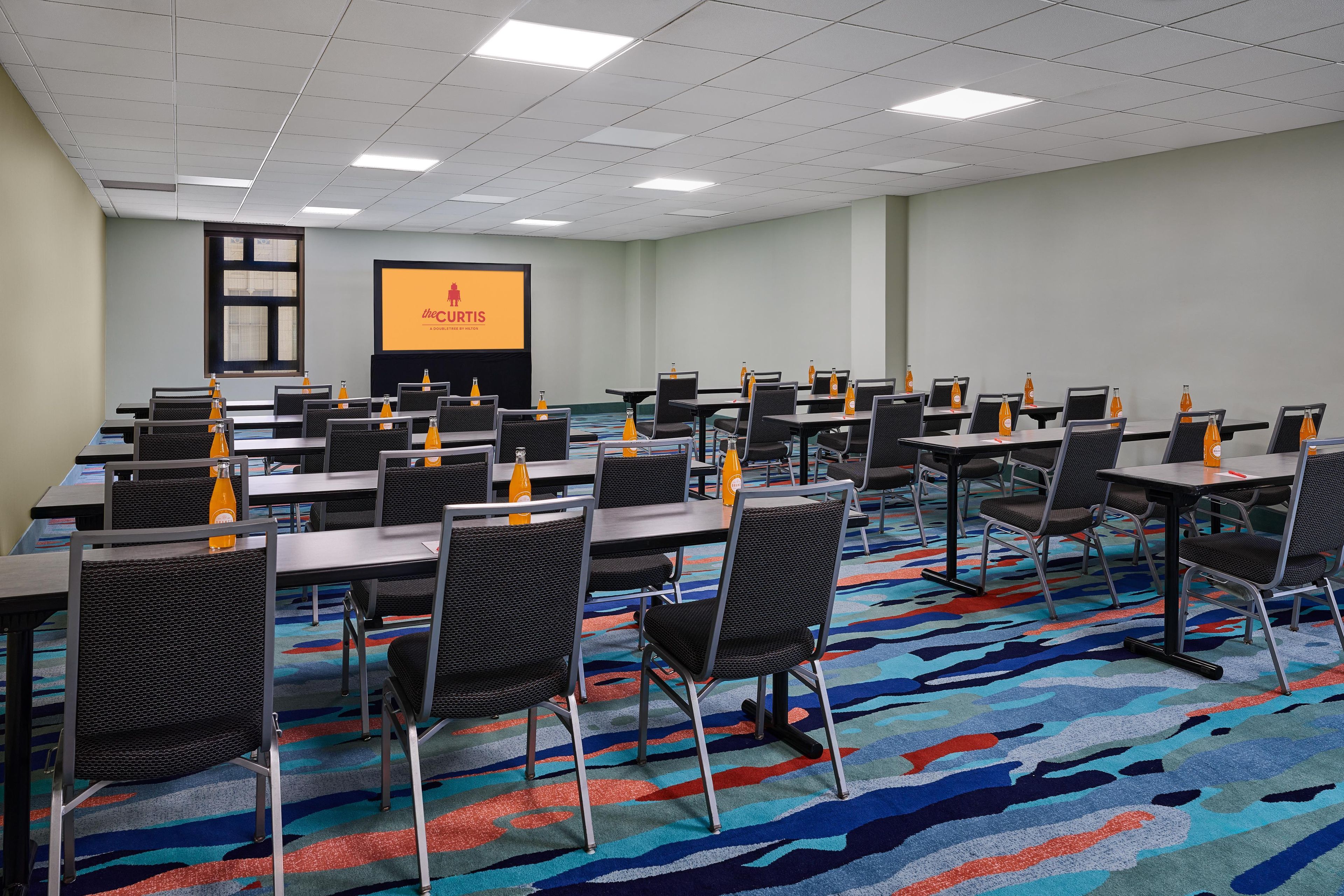 Un salón de conferencias con mesas, sillas y una pantalla de proyector.
