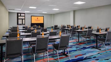 Un salón de conferencias con mesas, sillas y una pantalla de proyector.
