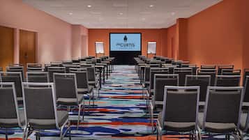 Une salle de conférence avec des rangées de chaises, un sol recouvert de moquette et un écran à l’avant sur lequel est affiché le nom « THE CURTIS A DOUBLEBREE BY HILTON ».