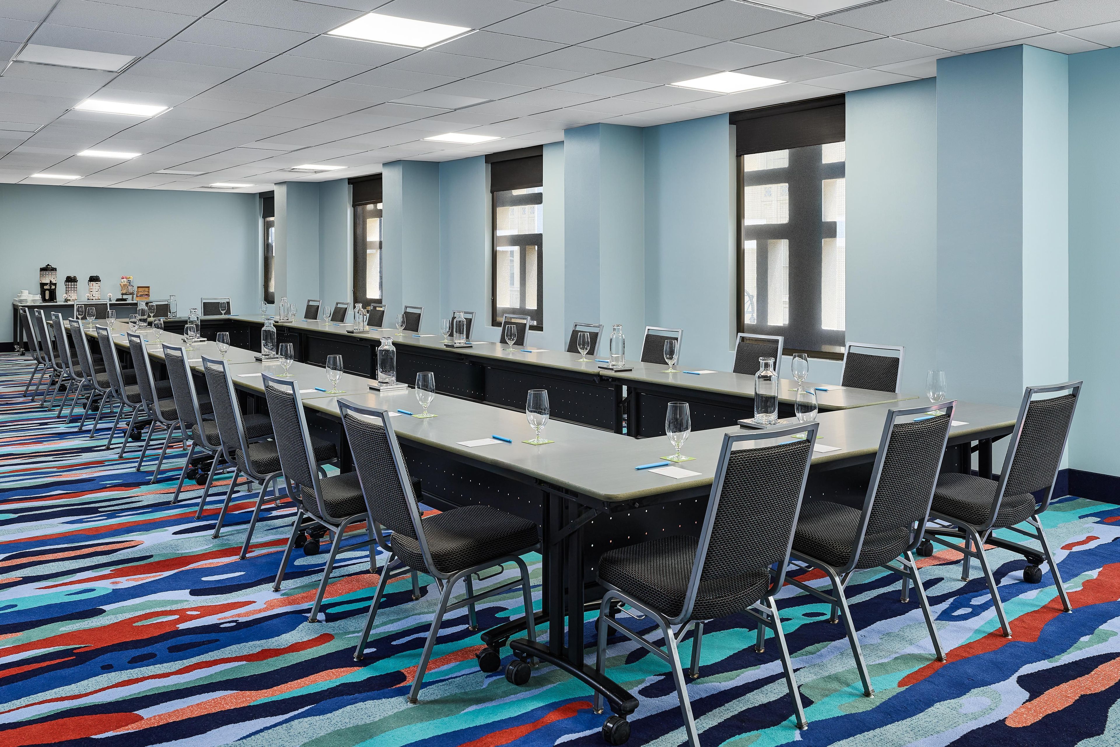 A conference room with long tables, chairs, and a colorful carpet.