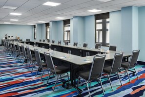 Un salón de conferencias con mesas largas, sillas y una alfombra colorida.