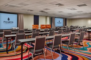 A conference room with multiple tables and chairs, a projector screen, and a carpeted floor. - the Curtis Denver - a DoubleTree by Hilton Hotel (Denver)