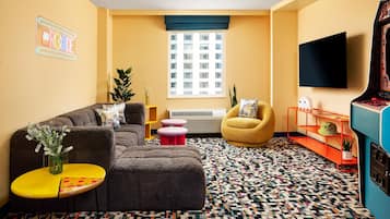 Un salon comprenant un canapé d’angle, une petite table ronde, un fauteuil jaune, un tapis à motifs et un téléviseur fixé au mur.