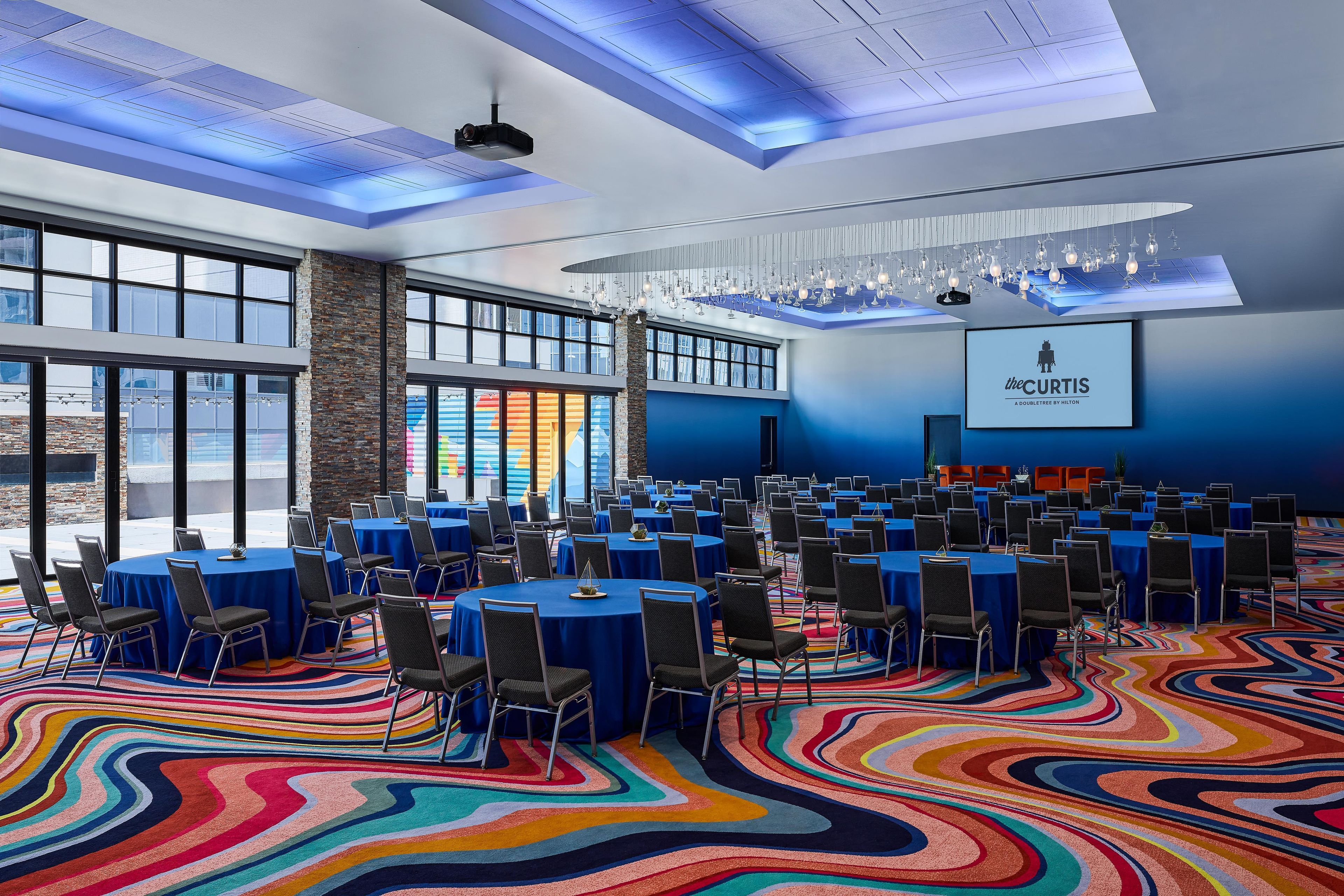 Un salón de conferencias con mesas redondas, sillas y una alfombra colorida.