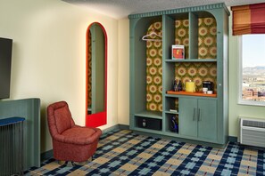 A room with a patterned carpet, a red chair, a wardrobe with floral wallpaper, and a view of a cityscape through a window. - the Curtis Denver - a DoubleTree by Hilton Hotel (Denver)