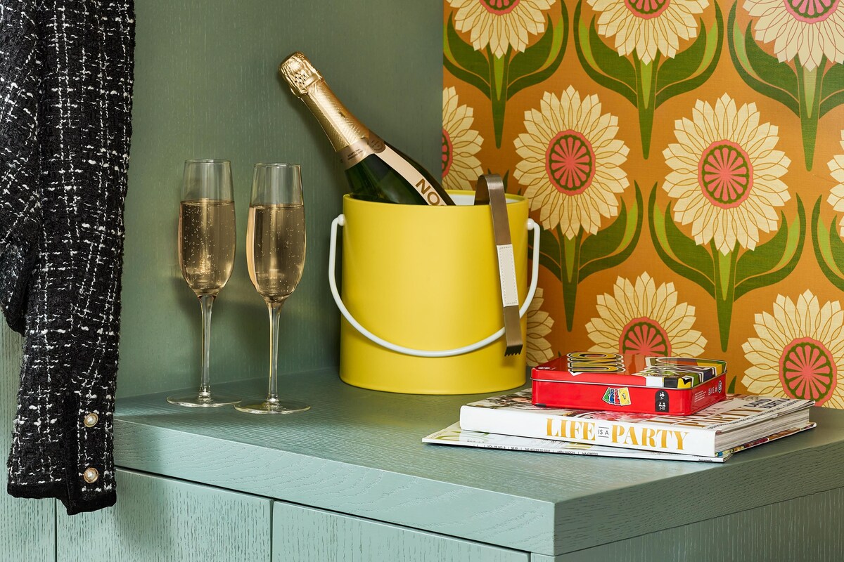 A table with two glasses of champagne, a yellow mug with a bottle, and a magazine titled 'Life is a Party'.