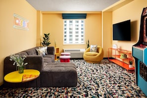 A living room with a sofa, a small table with a vase, a chair, a patterned rug, a window, and a television.