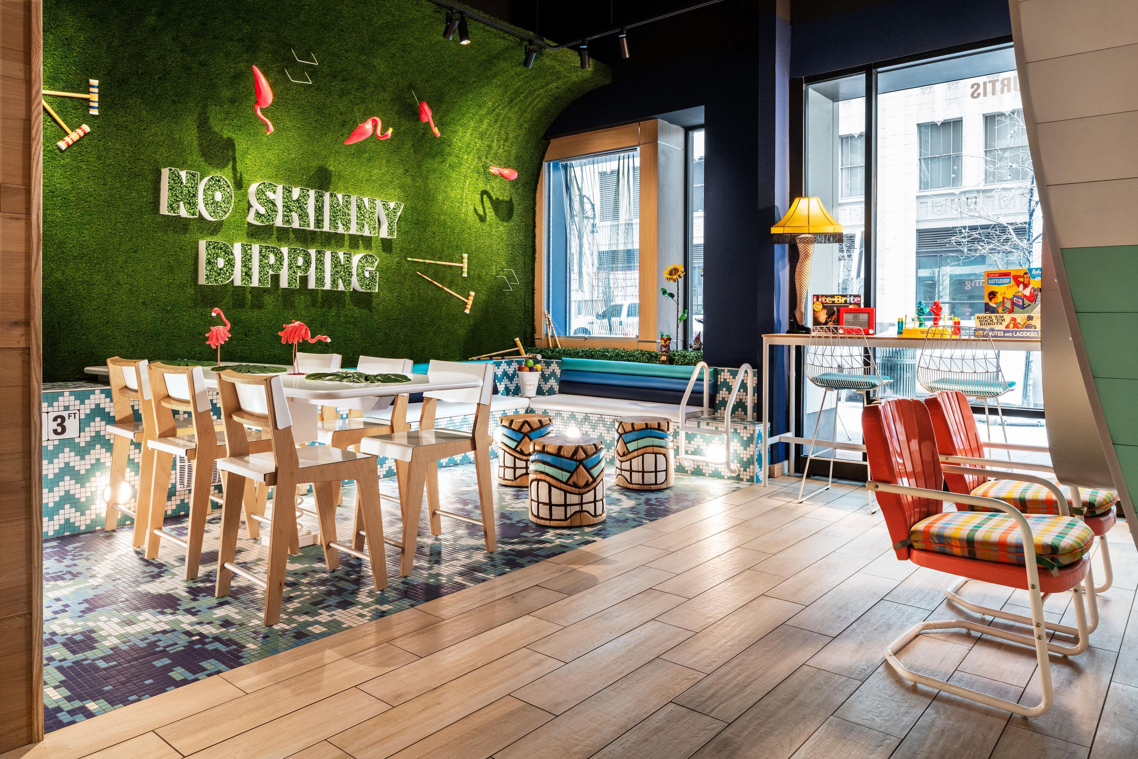 A modern lounge area with a green wall, wooden furniture, and a view of the city.