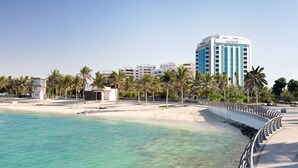 A beachfront hotel with a curved walkway, palm trees, and clear turquoise waters. - Sheraton Jeddah Hotel - Saudi Brothers Commercial Company Branch (Jeddah)