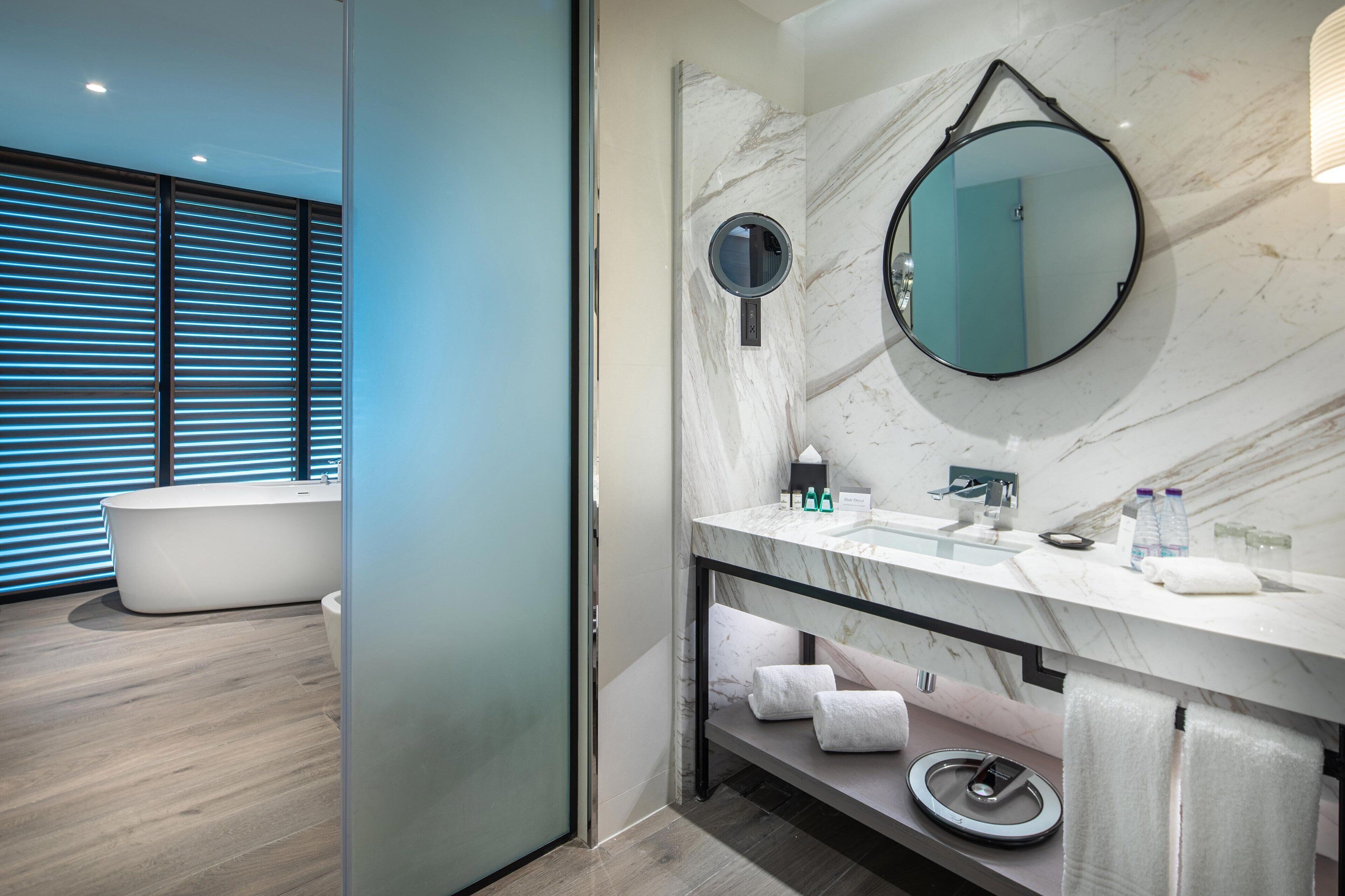 A modern bathroom with a freestanding bathtub, a marble vanity, a large mirror, and a towel rack.