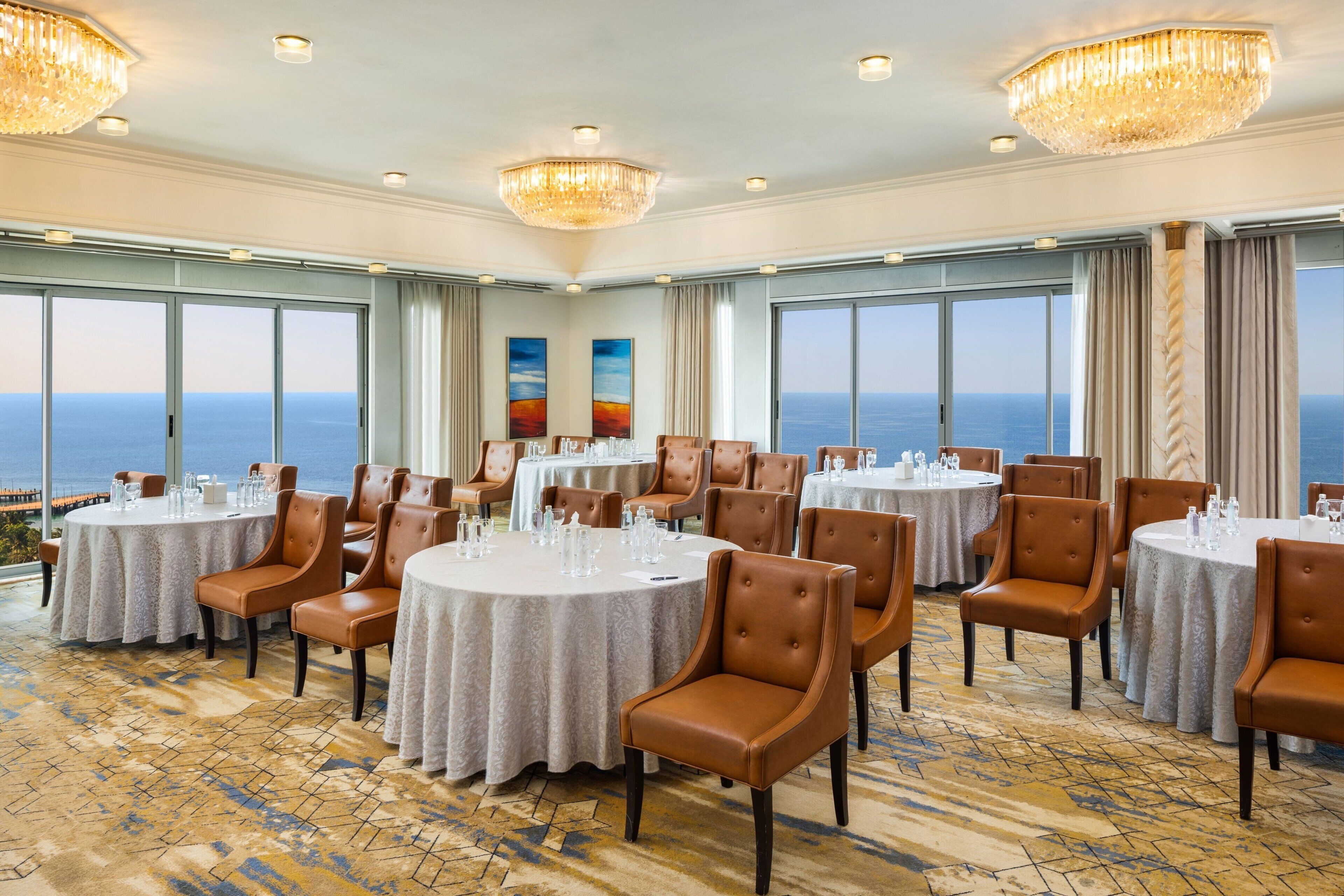A dining area with round tables, brown leather chairs, and large windows overlooking the ocean.