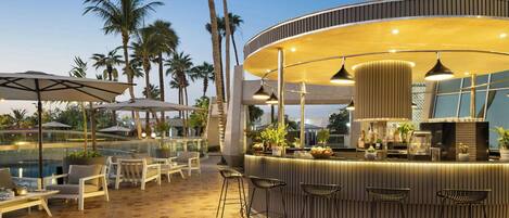 A bar area with a curved counter, bar stools, and a poolside seating arrangement with umbrellas.