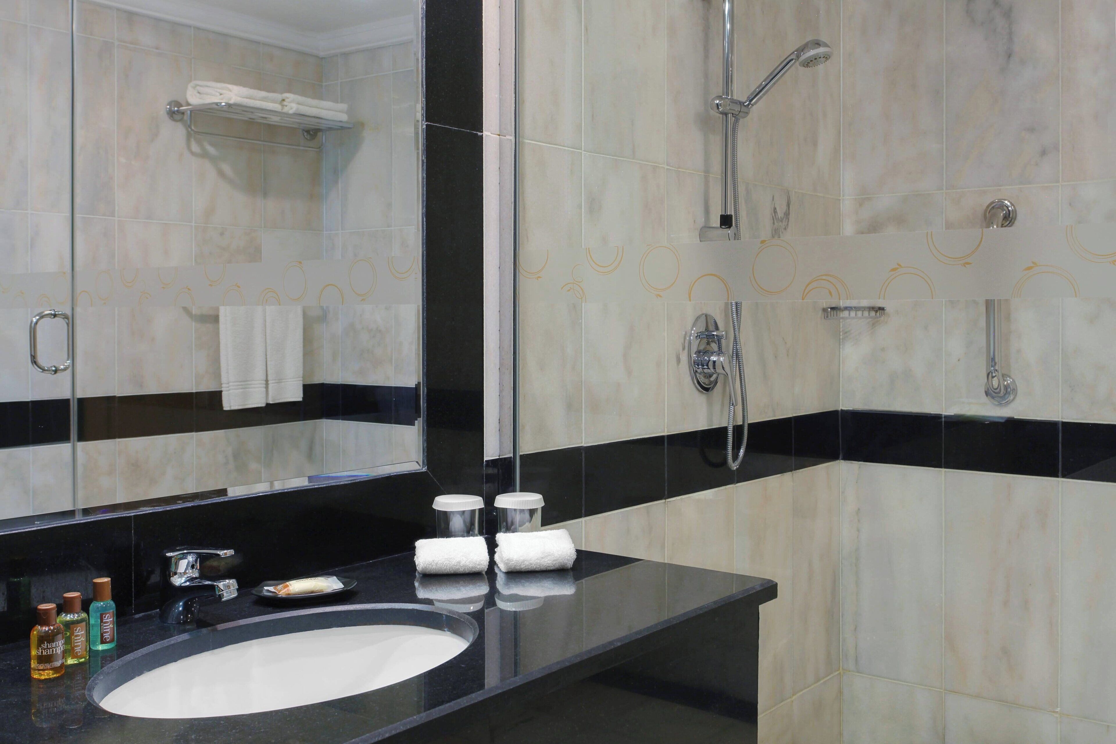 Un baño moderno con un espejo grande, una encimera negra, un lavabo y una zona de ducha.