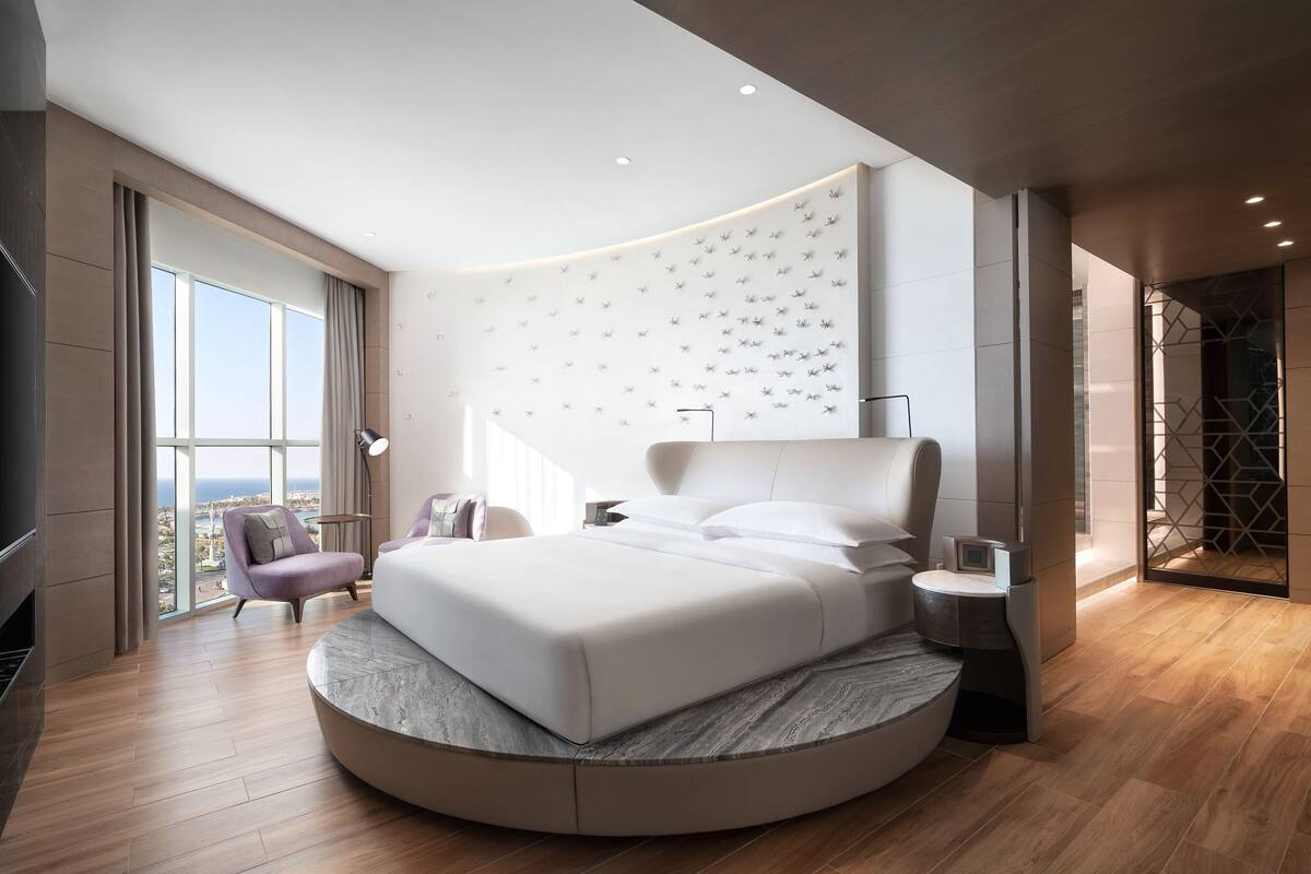 A modern bedroom with a curved bed, a large window, and a city view.