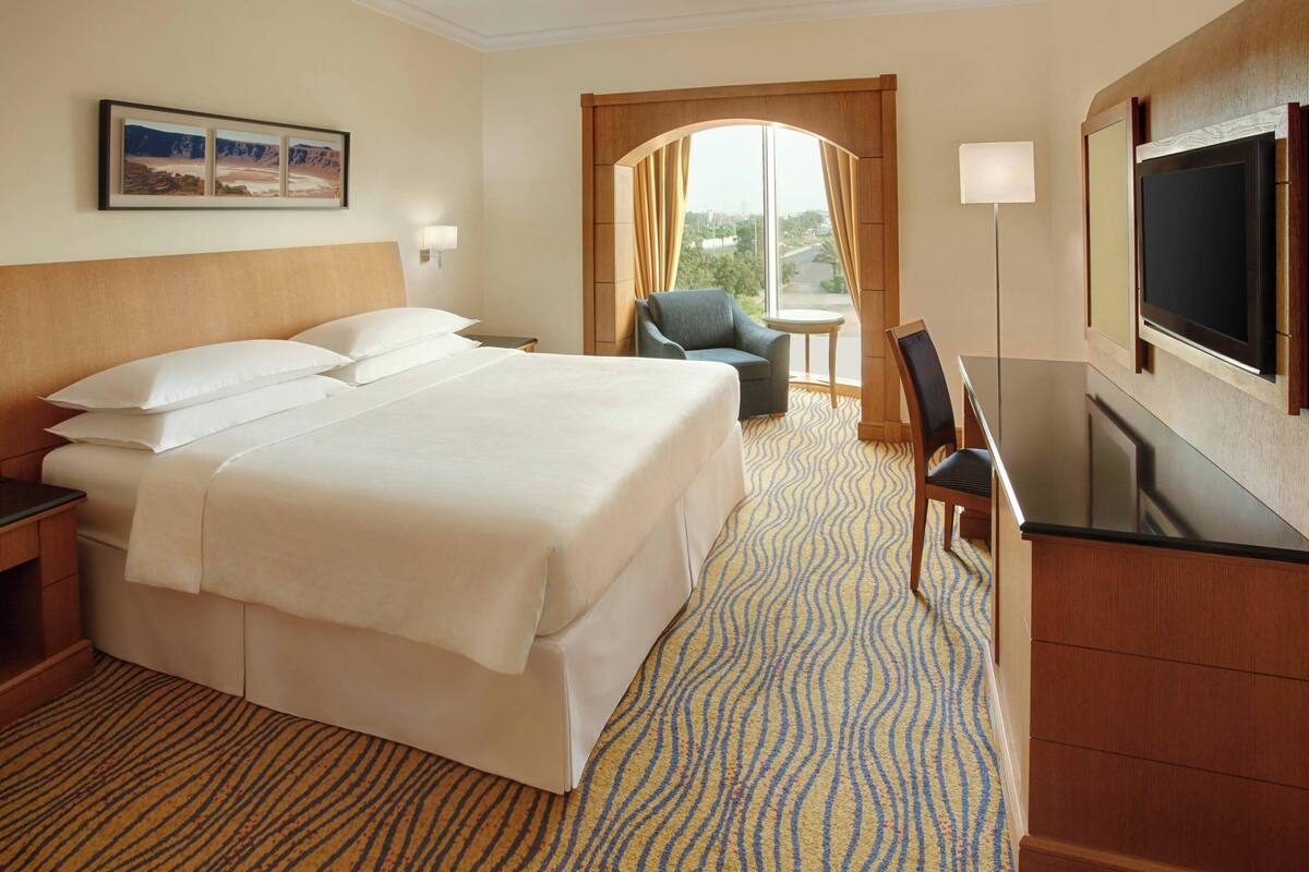 A hotel room with a large bed, a desk with a chair, a TV, and a window with curtains.
