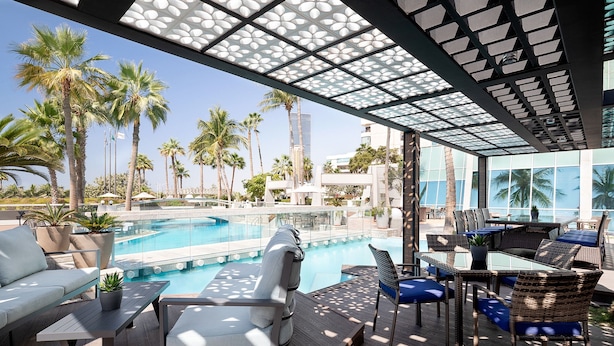 A poolside area with lounge chairs, a table, and a view of the pool and palm trees. - Sheraton Jeddah Hotel - Saudi Brothers Commercial Company Branch (Jeddah)