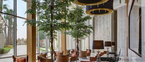 A spacious lobby with modern seating, a large central table, and large windows offering a view of palm trees.