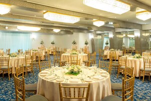 Un salón de banquetes con mesas redondas, sillas de madera y candelabros.