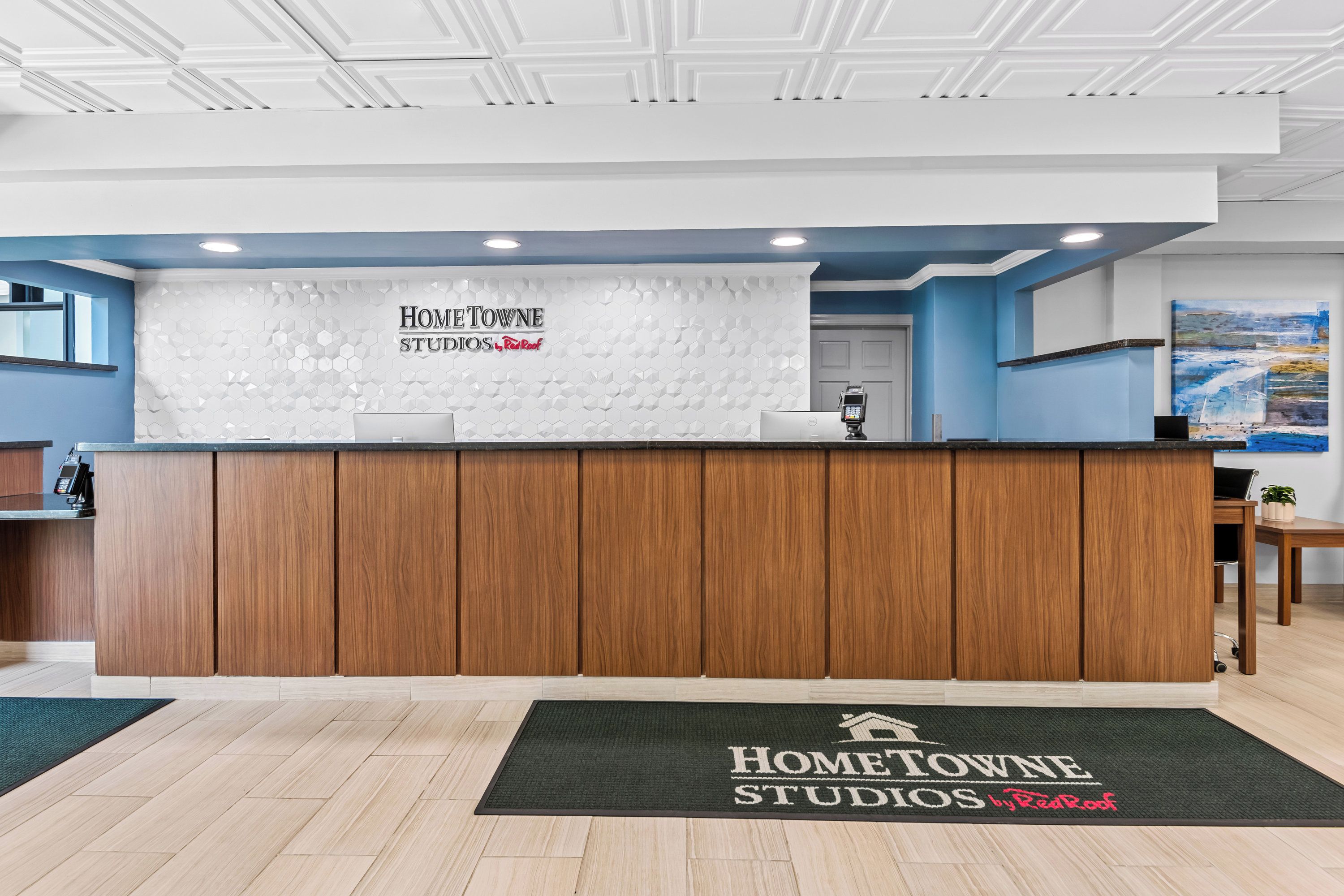 A reception area with a wooden reception desk, a digital payment terminal, and a reception desk mat with the property name.