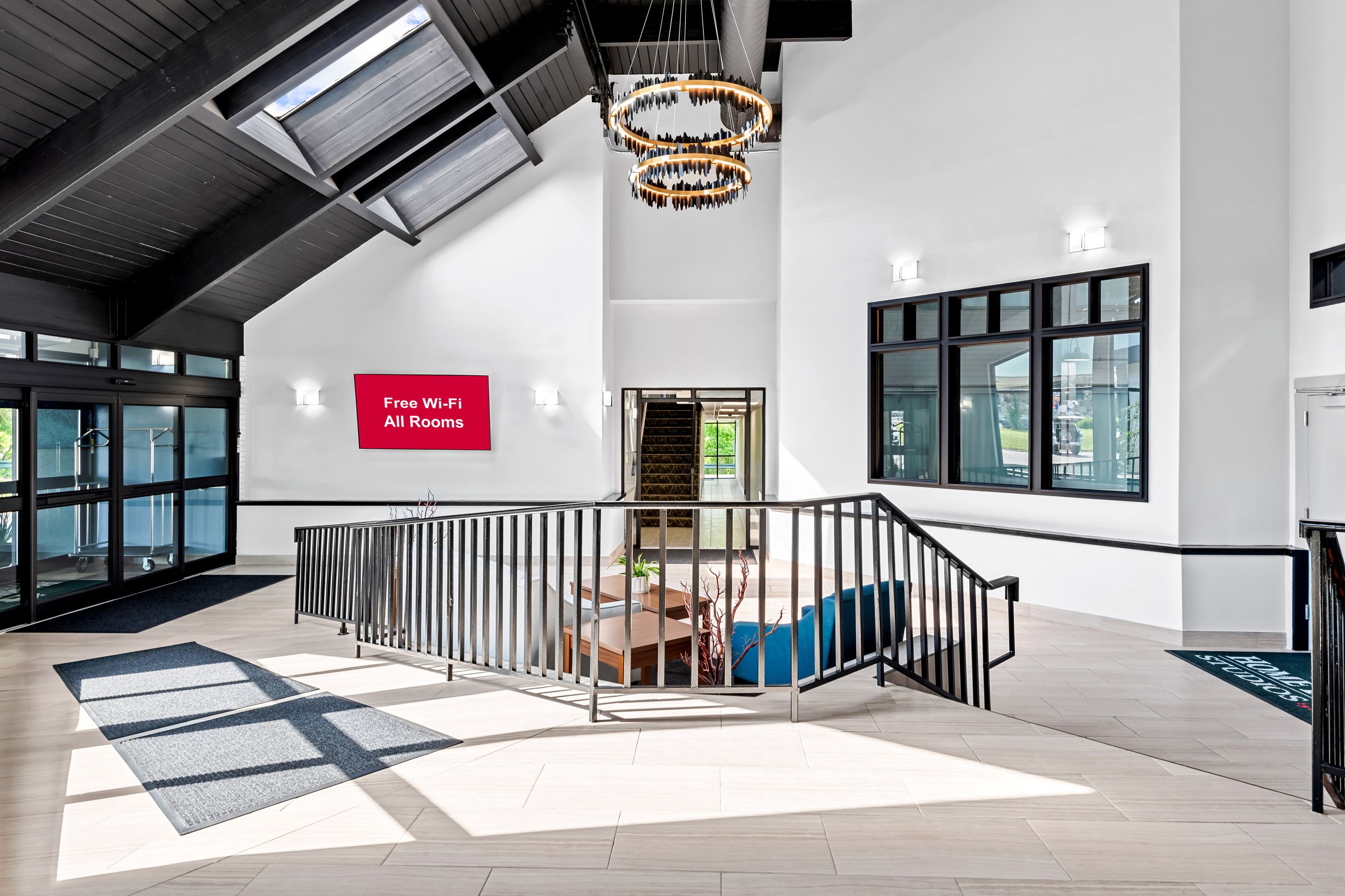 A modern hotel lobby with a staircase, a sign indicating free Wi-Fi, and large windows.