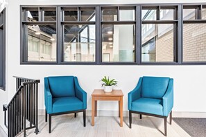 A modern interior with two blue armchairs, a small wooden table with a plant, and a large window with multiple panes. - HomeTowne Studios by Red Roof & Conference Center Cortland (Cortland)
