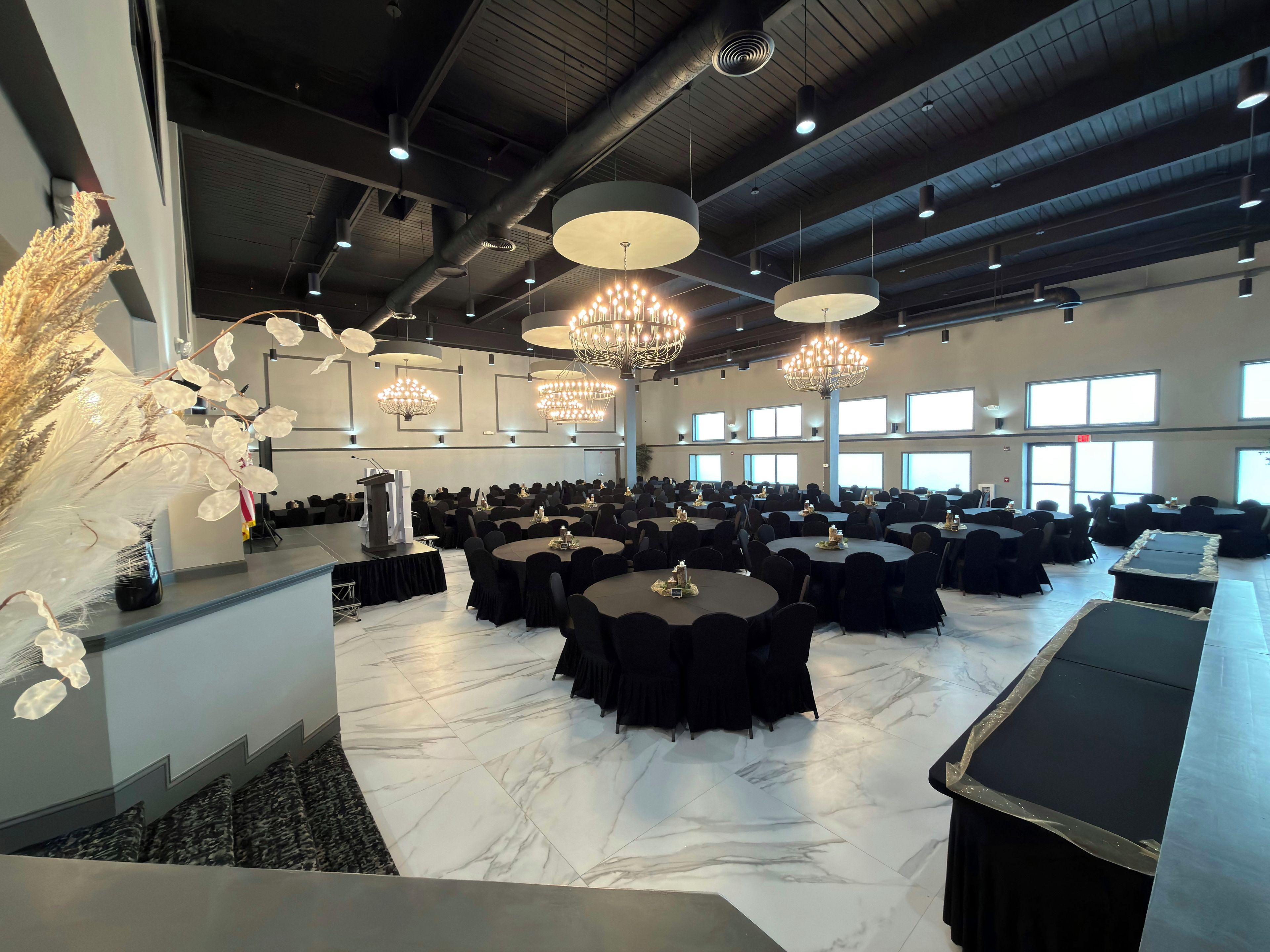 A large conference room with round tables, black chairs, and chandeliers.