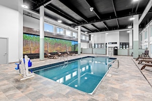 Una piscina interior con un mural, sillas de descanso y una zona junto a la piscina.