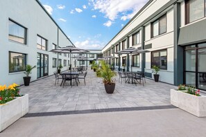 A courtyard with outdoor seating, potted plants, and a clear sky. - HomeTowne Studios by Red Roof & Conference Center Cortland (Cortland)