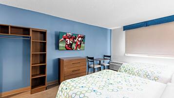 Habitación de hotel con cama, escritorio, silla, armario y televisor en la pared.