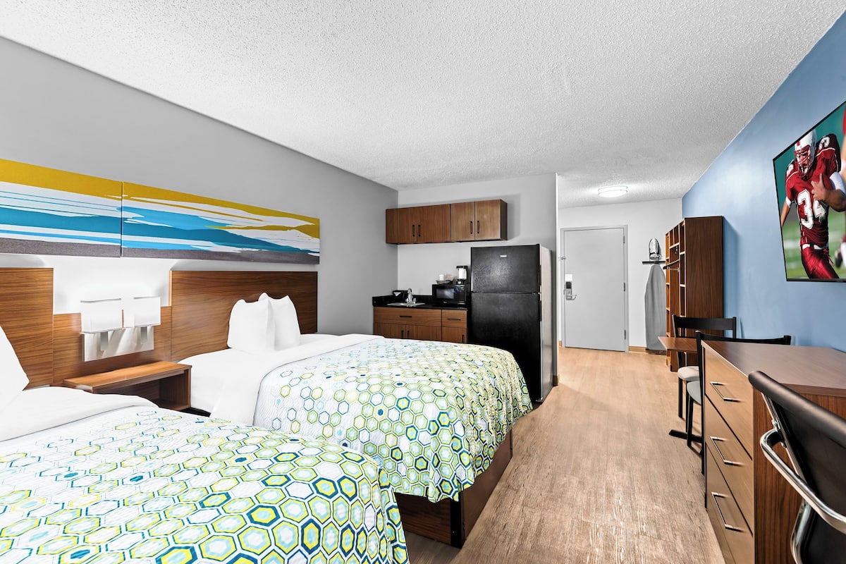 A hotel room with two beds, a kitchenette, a dining area, and a TV.
