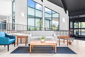 A modern lobby with a grey sofa, a blue armchair, a wooden coffee table, and a staircase with a black railing.