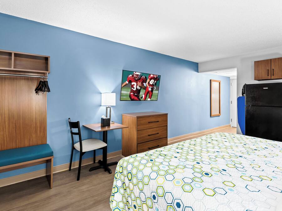 Habitación de hotel con cama, escritorio, silla, armario y refrigerador.