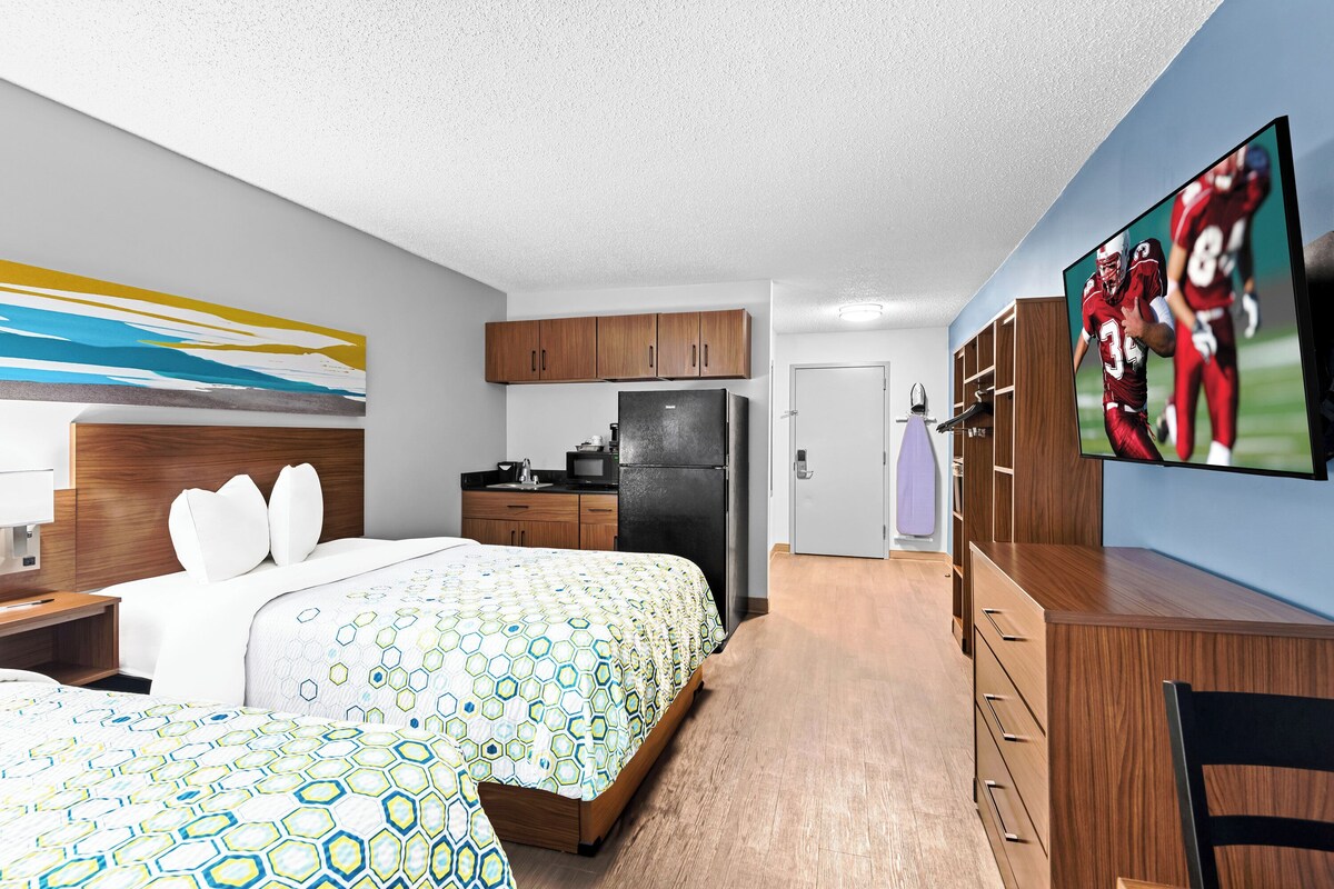 A hotel room with a bed, a desk, a TV, a kitchen area, and a bathroom.
