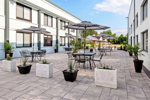 Un patio exterior con mesas, sillas, sombrillas y plantas en macetas.