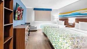 A hotel room with a bed, a desk, a chair, a window, and a painting on the wall. - HomeTowne Studios by Red Roof & Conference Center Cortland (Cortland)