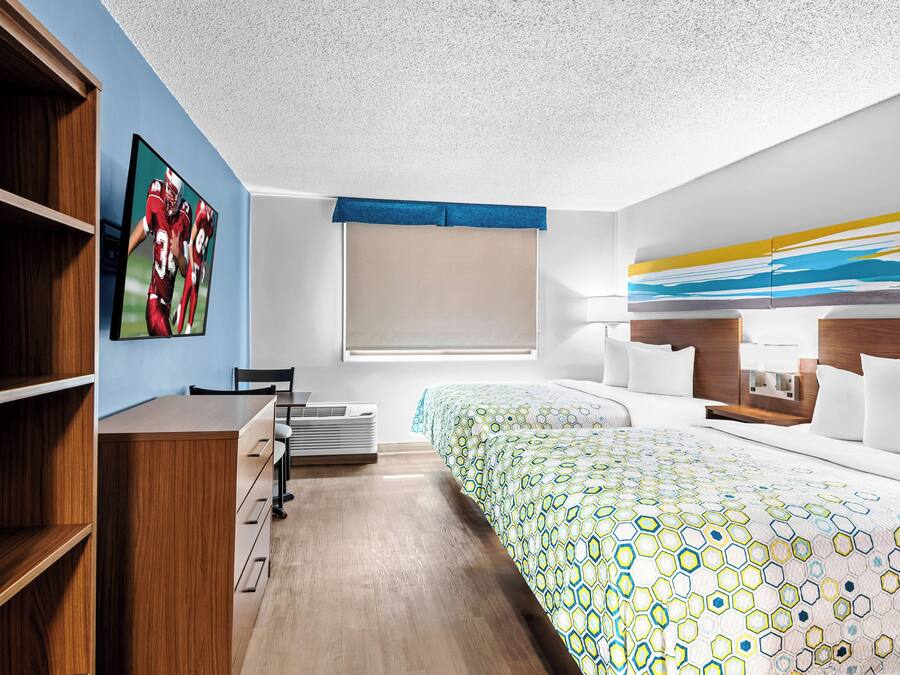 A hotel room with a bed, a desk, a chair, a window, and a painting on the wall.
