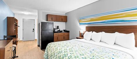 A hotel room with a large bed, a kitchenette, a wooden desk, and a modern abstract painting on the wall.