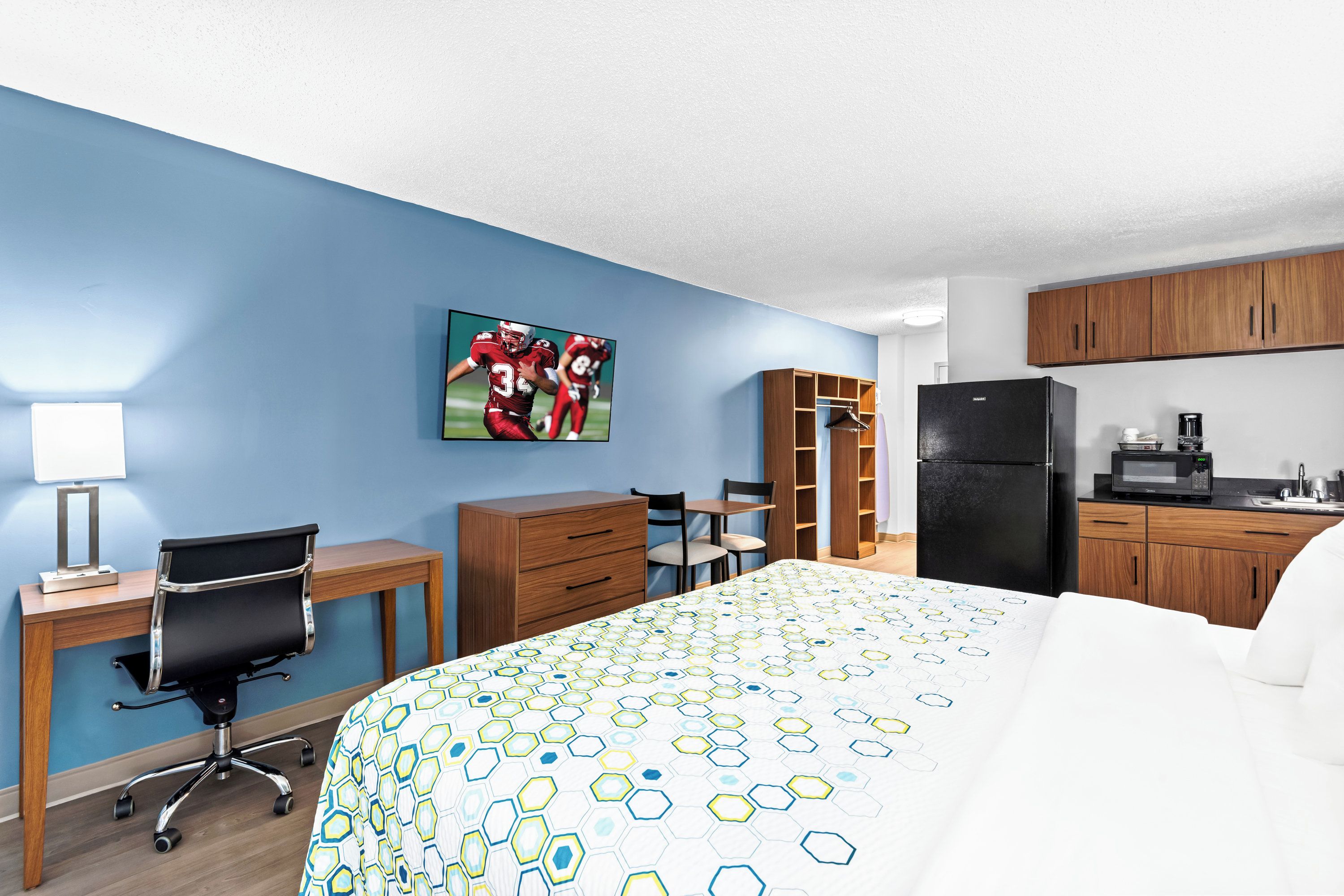 A hotel room with a bed, desk, chair, wardrobe, and kitchenette.