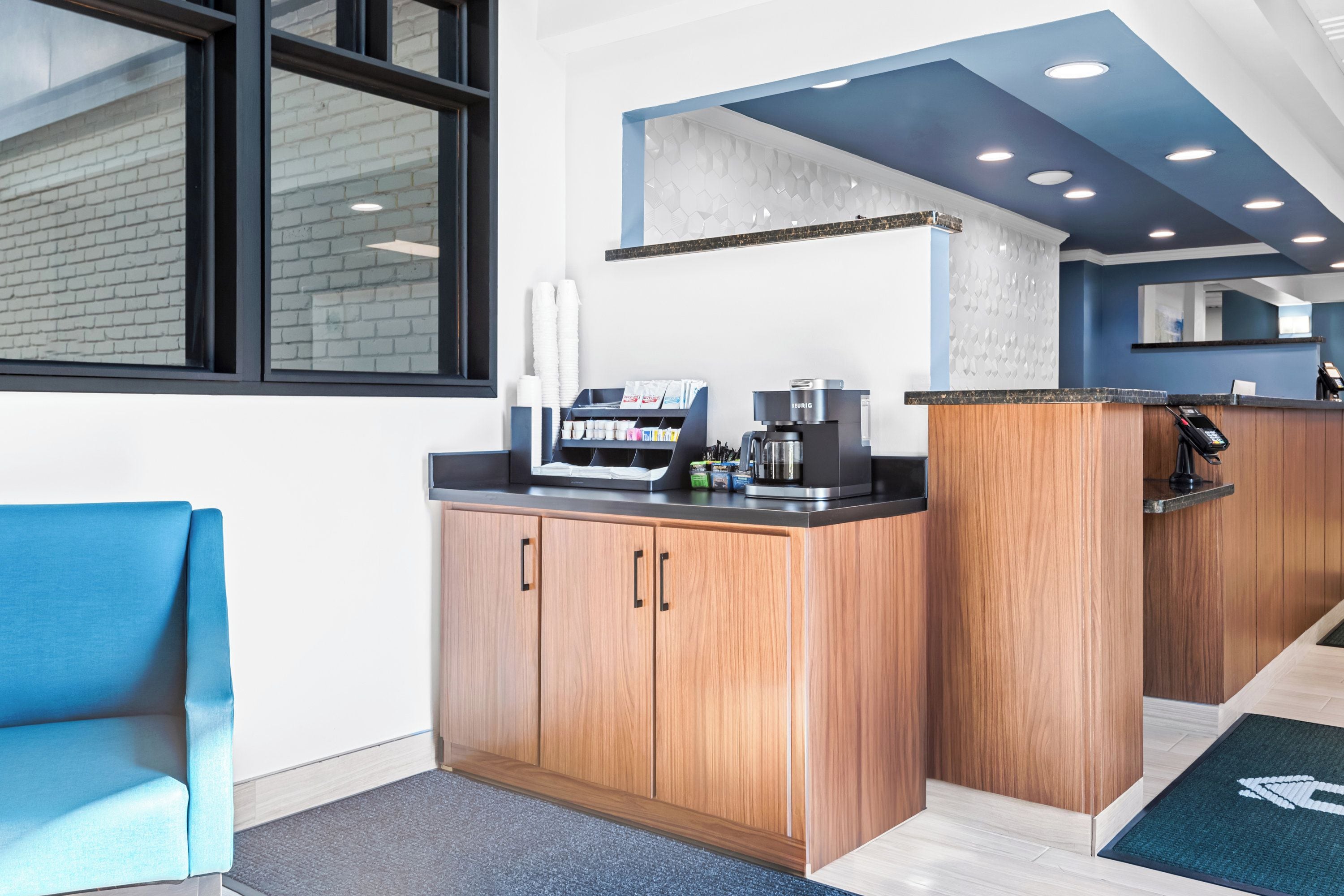 A modern kitchen area with wooden cabinets, a coffee machine, and a seating area with a blue chair.