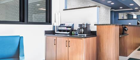 Un espace cuisine moderne avec des meubles en bois, une machine à café et un coin salon agrémenté d’une chaise bleue.