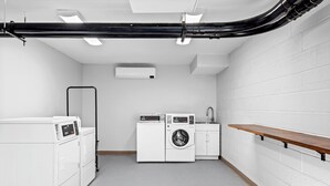 A laundry room with a washing machine, dryer, and a wooden shelf. - HomeTowne Studios by Red Roof & Conference Center Cortland (Cortland)