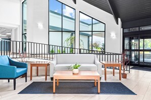 A modern lobby with a grey sofa, a blue armchair, a wooden coffee table, and a staircase with a black railing.