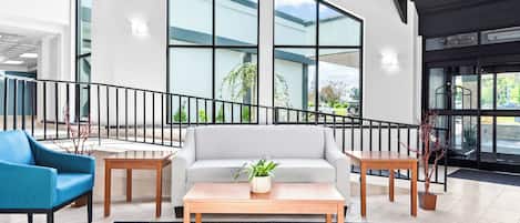 A modern lobby with a staircase, a sofa, a coffee table, and a blue armchair.