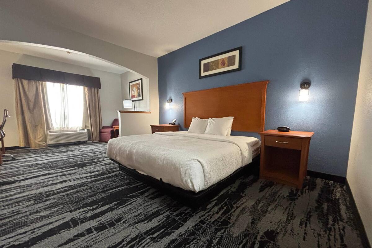 Een hotelkamer met een groot bed, een houten hoofdbord, twee nachtkastjes en een raam met gordijnen.